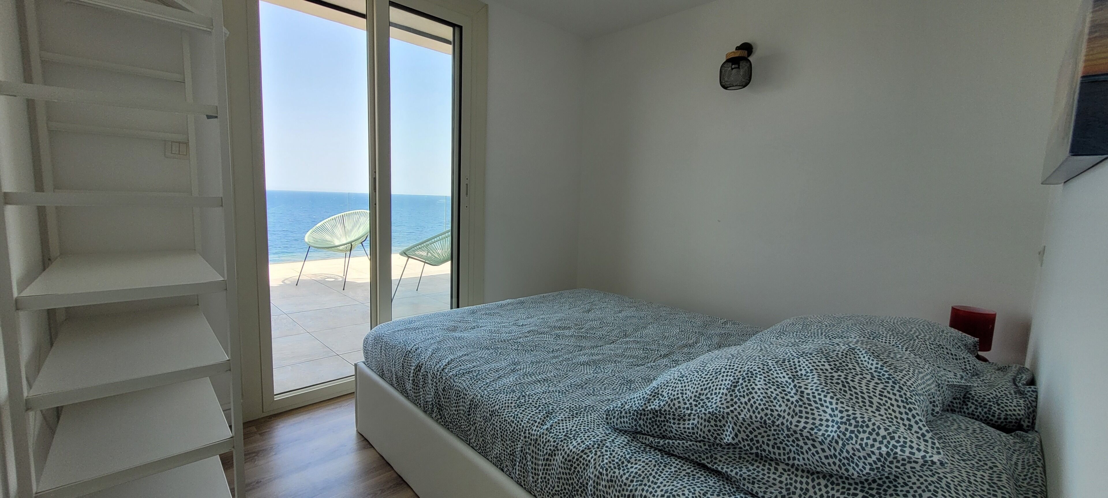 A bedroom with a bed, a wardrobe, and a view of the sea through a sliding door.