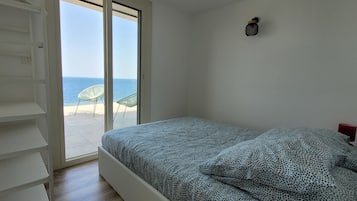 A bedroom with a bed, a wardrobe, and a view of the sea through a sliding door.