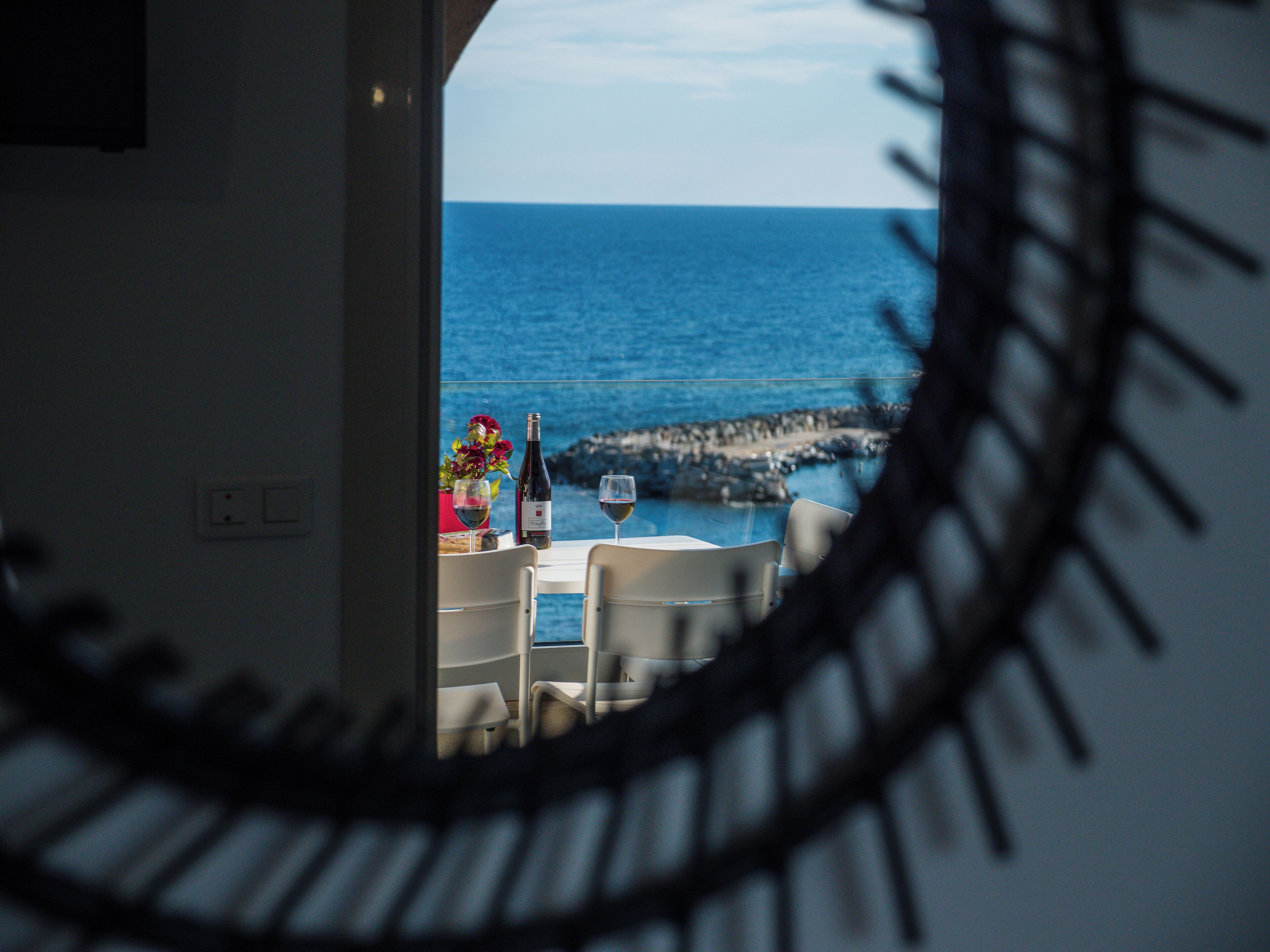 Een eethoek met uitzicht op zee door een rond raam.