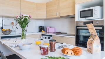 A kitchen with wooden cabinets, a microwave, an oven, a coffee maker, and a vase with flowers on the counter.