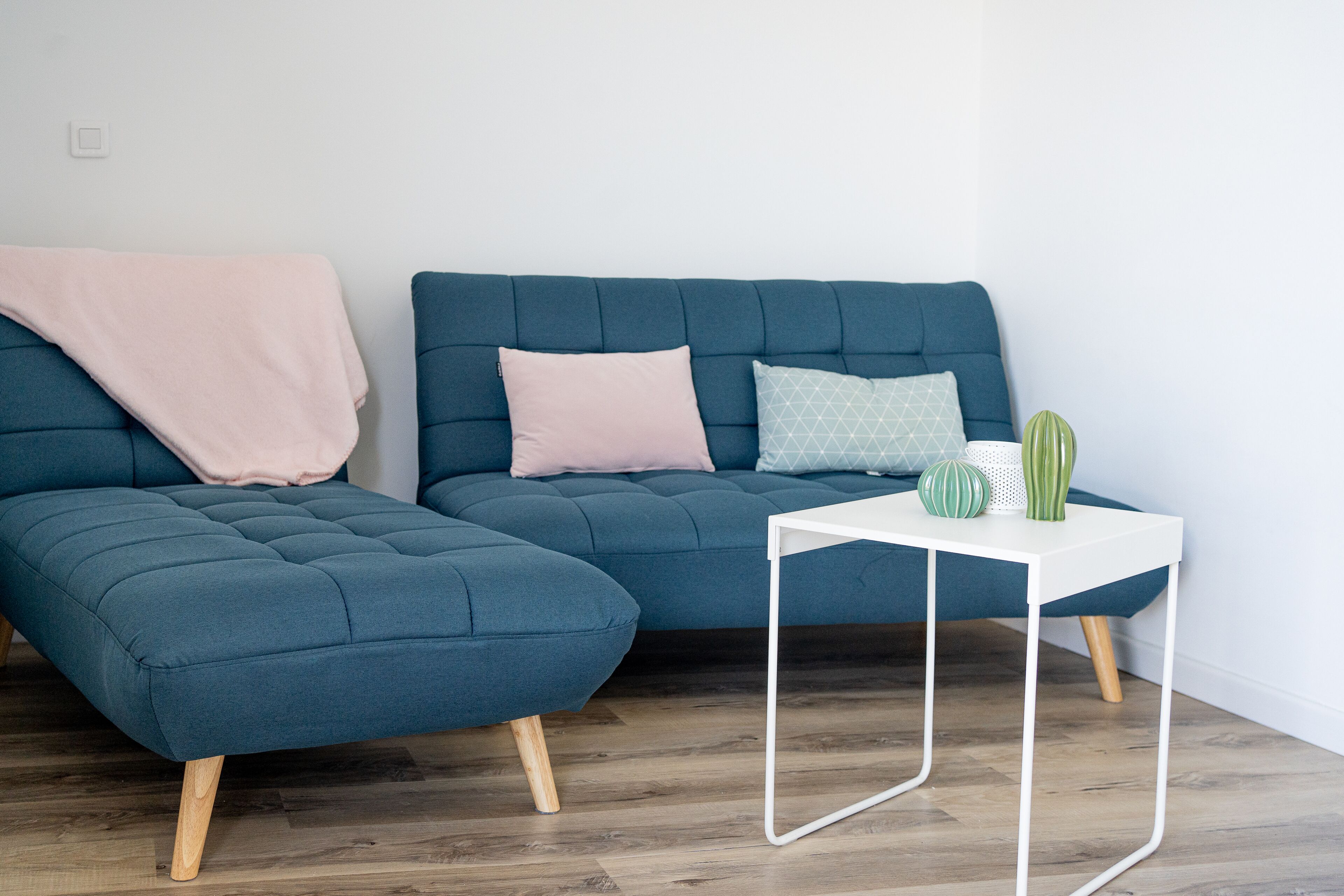 A modern living room with a blue sectional sofa, a small white side table, and a green cactus on the table.
