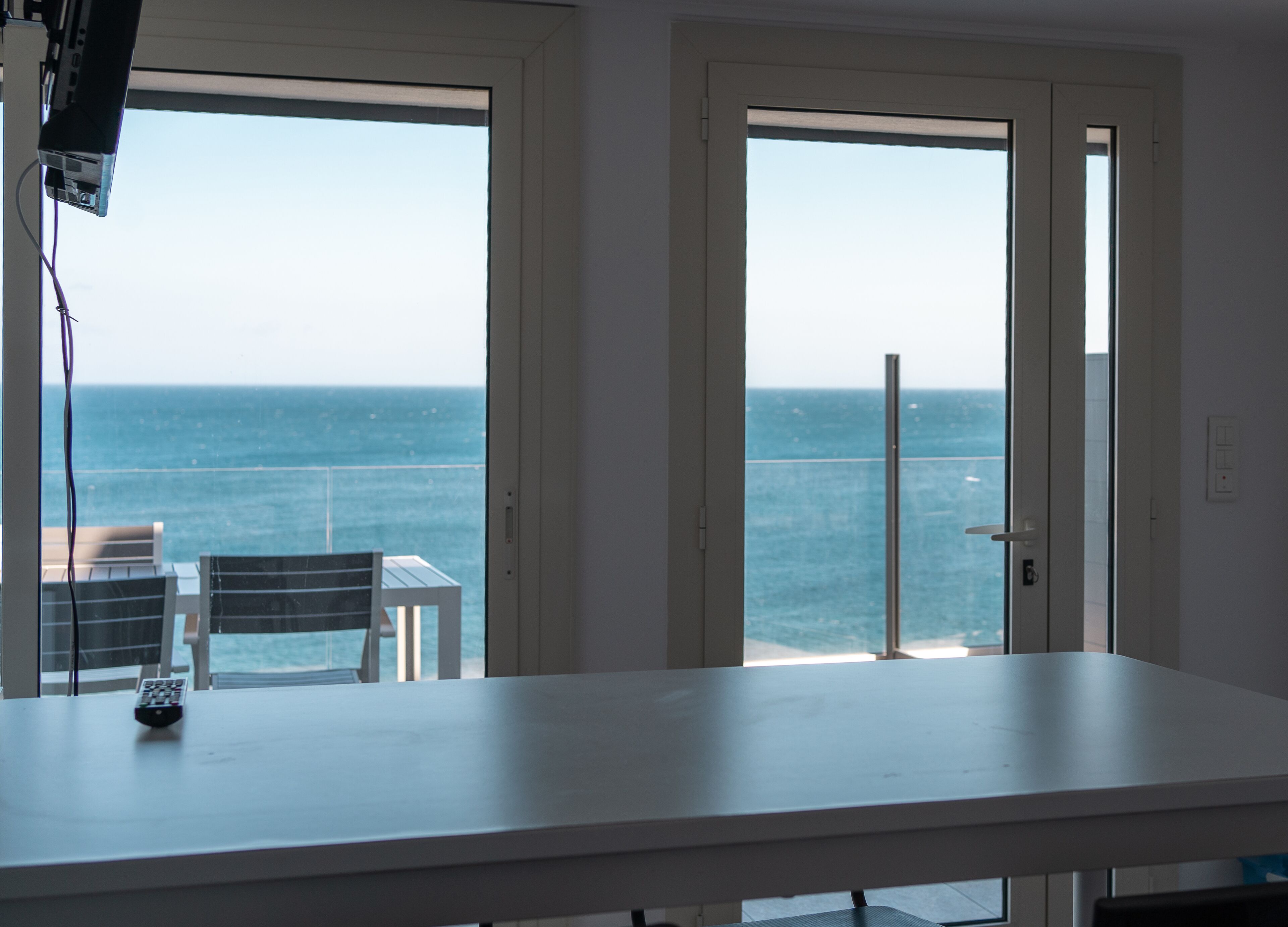 A room with a large window overlooking the sea, a white table, and a chair.