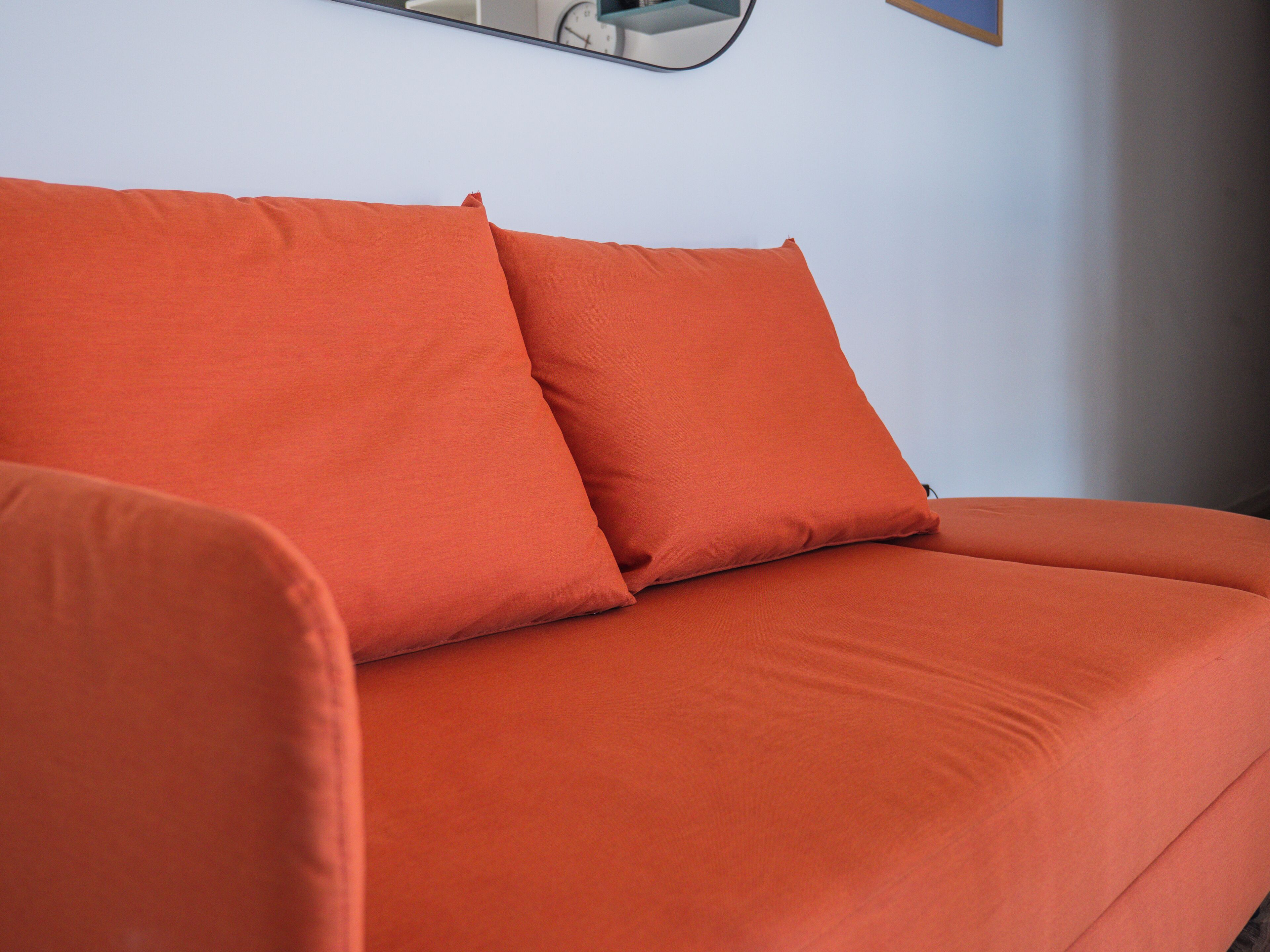 En modern, orange soffa placerad framför en vit vägg, med en klocka på väggen.