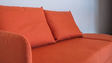 En modern, orange soffa placerad framför en vit vägg, med en klocka på väggen.