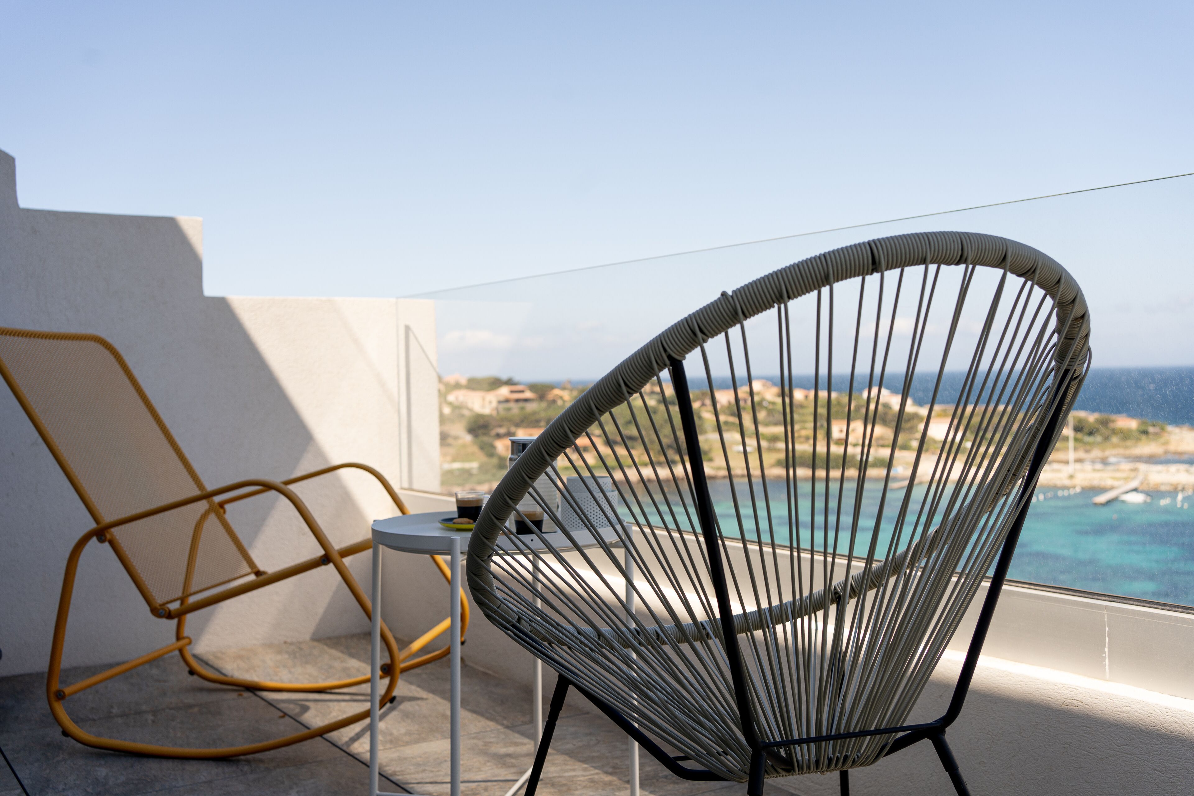 A balcony with a view of the sea, a wicker chair, and a small table.