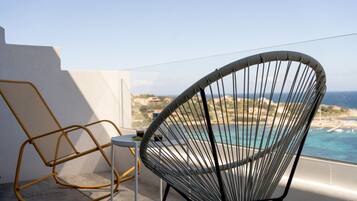 A balcony with a view of the sea, a wicker chair, and a small table.