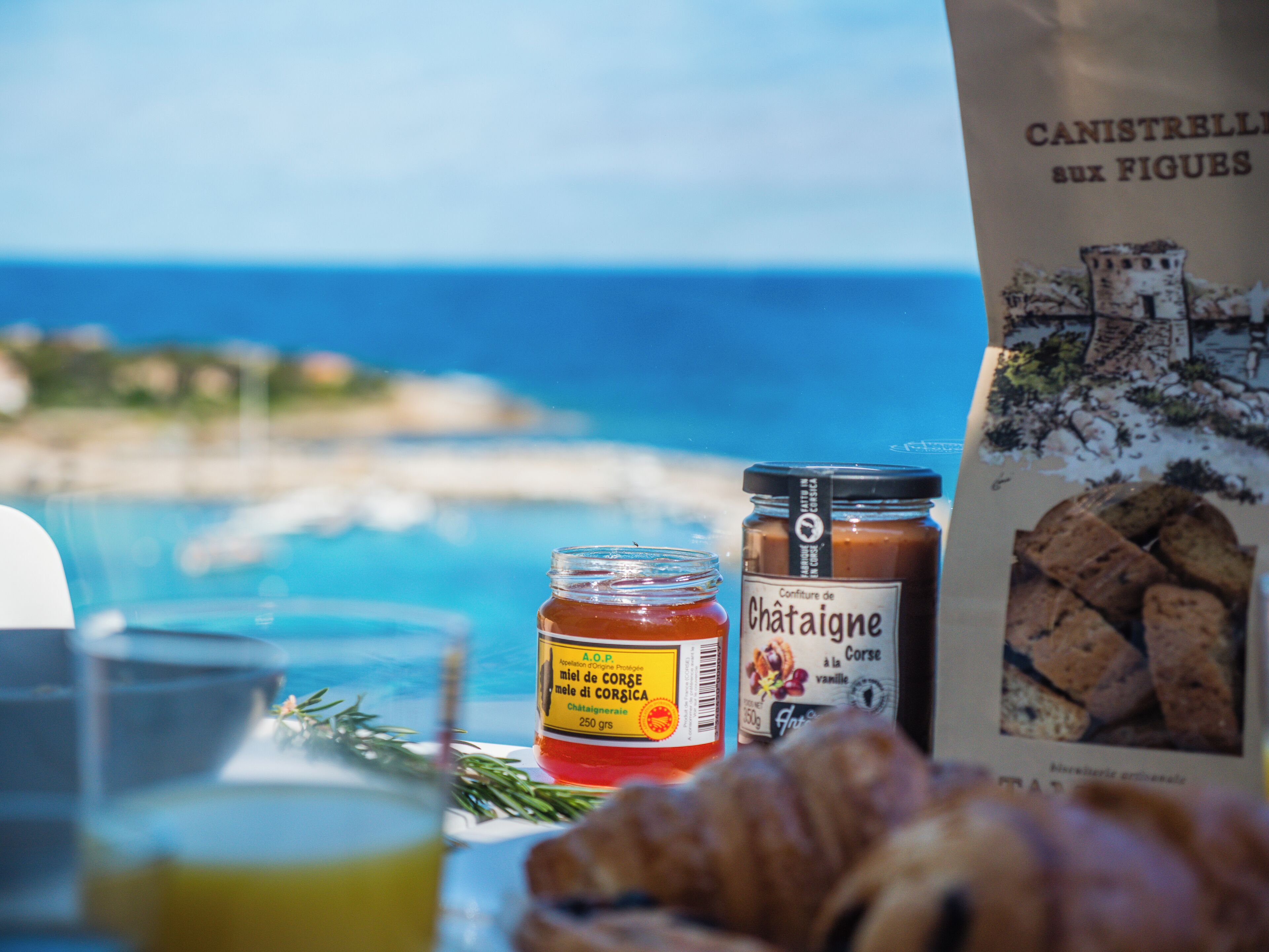 A table with a jar of honey, a bottle of jam, and a bag of biscuits.