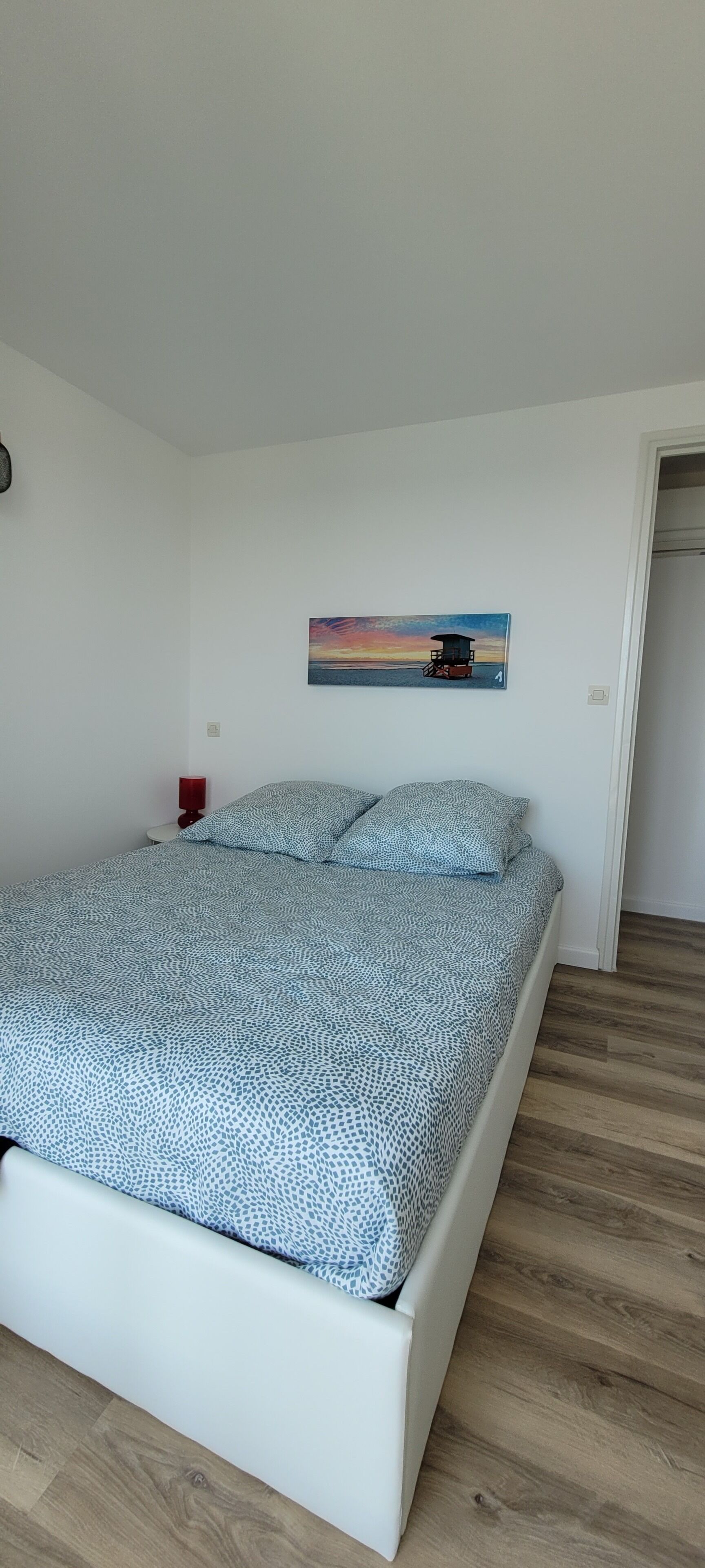 Une chambre à coucher avec un lit, une table de chevet, un tableau et un plancher en bois.