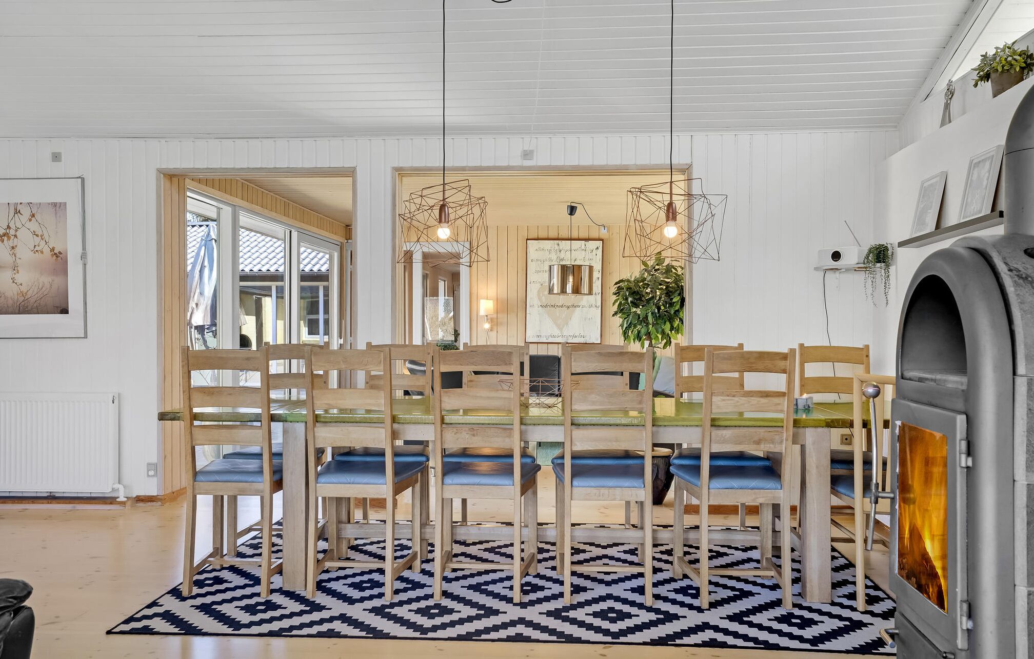 Un comedor con sillas de madera y una mesa de vidrio, un tapete estampado y una cocina moderna con horno empotrado.