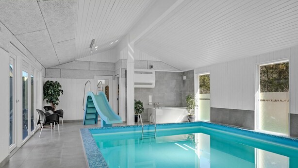 An indoor swimming pool with a slide, a shower area, and seating by the pool. - Gorgeous home in Blokhus with sauna (Blokhus)