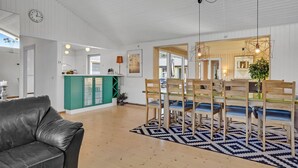 A spacious living area with a leather sofa, a dining table with wooden chairs, a patterned rug, and a kitchen area with green cabinets and a white countertop. - Gorgeous home in Blokhus with sauna (Blokhus)