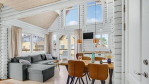 Ein gemütliches Wohnzimmer mit einer Couch, einem Esstisch mit Stühlen und einer Küchenzeile mit Fernseher und Pendelleuchten.