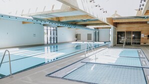 Uma piscina interior ampla com várias pistas de natação, teto de madeira e entrada por porta de vidro.
