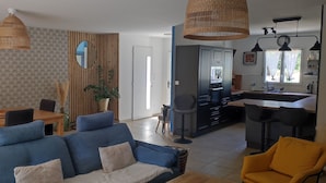 A modern living room with a blue sofa, dining table, and kitchen area. - House close to activities and tourist sites (Labastide-de-Virac)