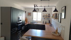 A modern kitchen with dark cabinetry, a wooden island, pendant lighting, and a view of the living area. - House close to activities and tourist sites (Labastide-de-Virac)