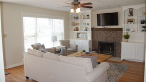 A living room with a white sofa, a coffee table, a fireplace, and a TV mounted above it. - Sandy Neighborhood Private Beach Getaway in Huron (Huron)