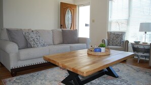 A living room with a grey sofa, a wooden coffee table, and a patterned rug. - Sandy Neighborhood Private Beach Getaway in Huron (Huron)