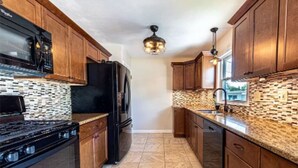 A kitchen with wooden cabinets, a black refrigerator, a stove, and a patterned backsplash. - Sandy Neighborhood Private Beach Getaway in Huron (Huron)