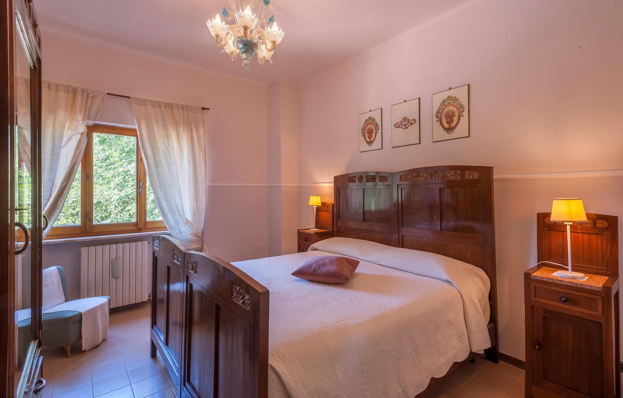 A bedroom with a wooden bed, two bedside lamps, a window with curtains, and a radiator.