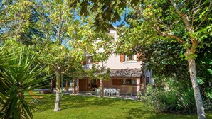 Ein zweigeschossiges Haus mit einer überdachten Terrasse, umgeben von üppiger Vegetation und Bäumen.