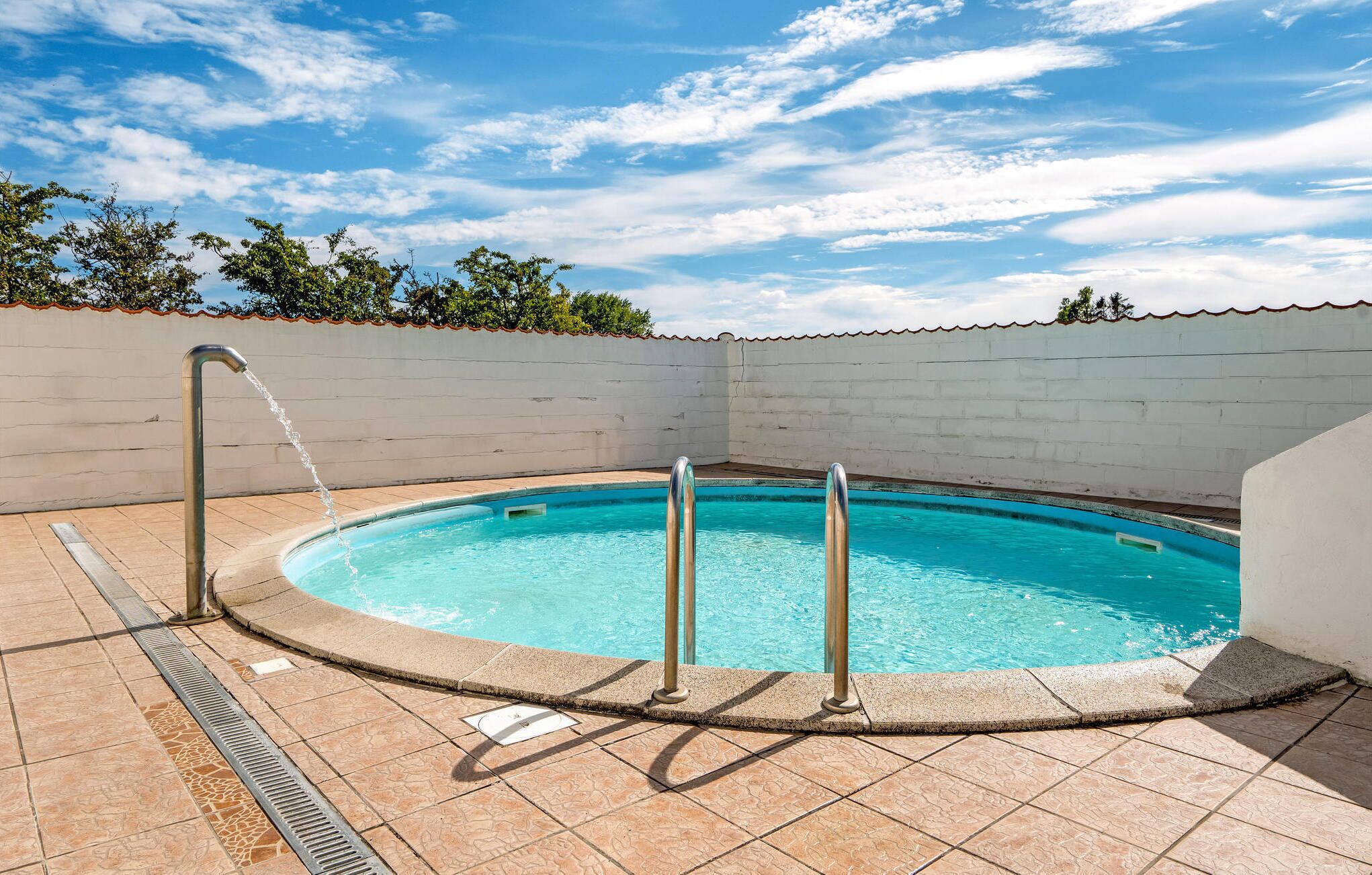 Une petite piscine ronde, dotée d’une terrasse carrelée et d’échelles en métal.