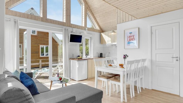 A modern, well-lit room with a grey sofa, white dining table, and a kitchen area. - Pet friendly home in Tranekær with WiFi (Tranekær)
