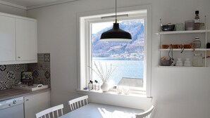 Una cocina con una mesa de comedor, armarios blancos, un ventanal con vistas a un lago y una lámpara colgante.