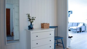 Una habitación con un aparador blanco, una silla azul y una cesta de mimbre sobre una mesa blanca.