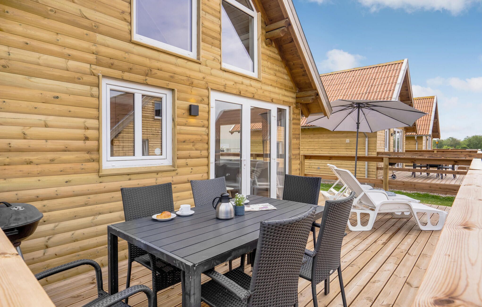 A wooden cabin with a deck, outdoor seating, and a grill.