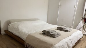 A neatly made bed with a white comforter and two folded towels on a wooden platform bed in a room with wooden flooring. - Charming Apartment Garden View (London)
