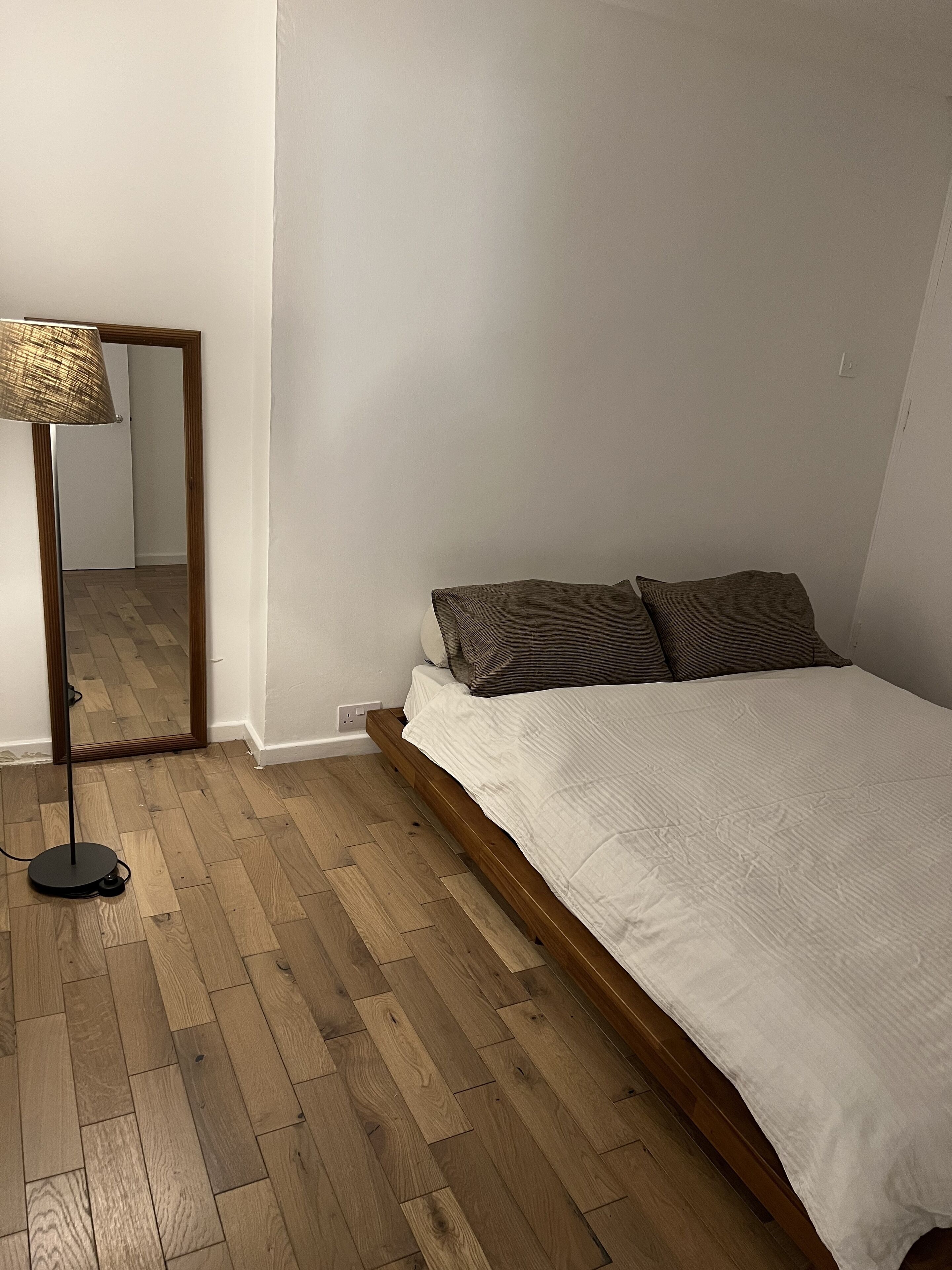 A bedroom with a wooden floor, a bed with white bedding, and a floor lamp.