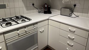 A kitchen with white cabinets, a gas stove, a coffee maker, and a toaster. - Charming Apartment Garden View (London)