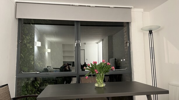 A dining area with a table, chairs, a vase with flowers, a window with blinds, and a tall floor lamp. - Charming Apartment Garden View (London)