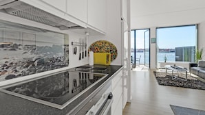 A modern kitchen with a large island, a view of the sea through a window, and a dining area with a view of the city. - Amazing apartment in Korsør (Korsør)