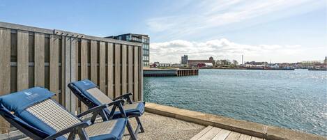 Eine Terrasse mit Liegestühlen und Blick auf einen Fluss sowie Gebäude im Hintergrund.
