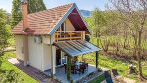 Una casa a due piani con tetto spiovente, un portico coperto con tavolo e sedie, e vista su una zona boschiva.