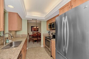 A kitchen with a stainless steel refrigerator, a microwave, and a stove. There is a dining area with a table and chairs.