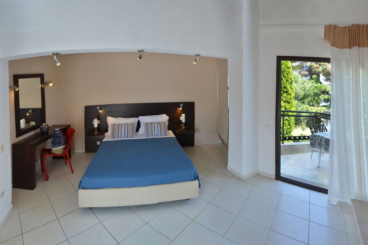 A bedroom with a bed, a desk, a chair, a window, and a balcony.