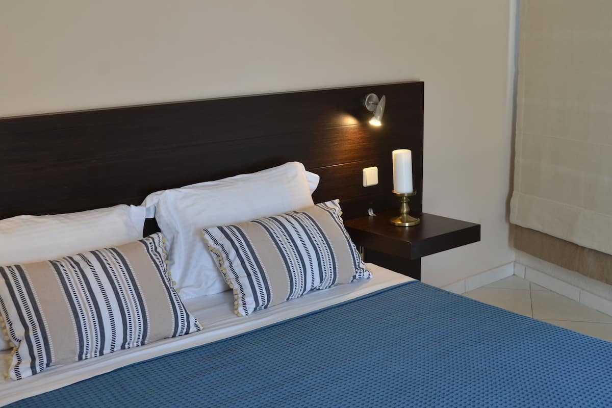 A neatly made bed with striped pillows, a blue bedspread, and a bedside table with a candle.