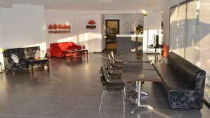 Eine moderne Hotelhalle mit einer Rezeption, einer Sitzgelegenheit und Blick auf die Küche.