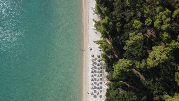 Eine Vogelperspektive zeigt einen Strand mit mehreren Reihen Sonnenschirmen und Badegästen.