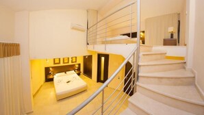 Ein Schlafzimmer mit Bett, Nachttisch, Kommode, Spiegel und einer Treppe.