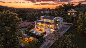 A modern two-story house with a swimming pool, surrounded by lush greenery and a sunset view. - Luxury Estate with Heated Pool & el Yunque Views (Luquillo)