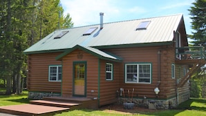 A log cabin with a metal roof, a front porch, and a stone foundation.