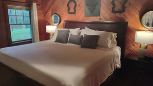 A wooden-paneled bedroom with a large bed, two bedside lamps, and a window with curtains.
