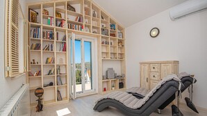 Ein Wintergarten mit Liege, einer großen Bücherwand und Blick durch eine Glastür.