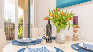 Ein Esstisch ist gedeckt mit blau-weißen Streifen Tischsets, Tellern und Weingläsern, dazu eine Weinflasche und ein Strauß Tulpen.