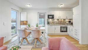 Eine moderne Küche mit weißen Schränken, einem eingebauten Ofen und einer Mikrowelle. Ein Essbereich mit Tisch und Stühlen lädt zum Verweilen ein, und große Fenster bieten einen Blick auf einen See.