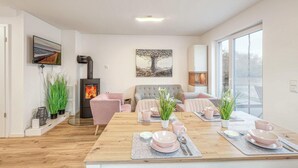 Ein modernes Wohnzimmer mit Kamin, einem Essbereich für vier Personen und einem großen Fenster, das natürliches Licht hereinlässt.
