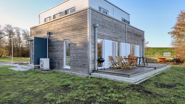 Ein modernes, zweistöckiges Haus mit überdachter Terrasse, Sitzgelegenheit im Freien und einem sichtbaren Schornstein.